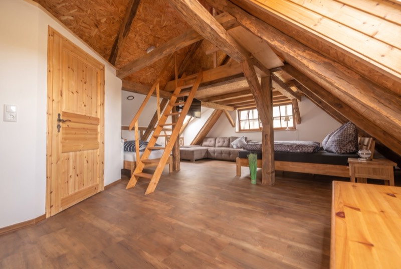 Dachzimmer mit offenem Gebälk und Leiter zur oberen Schlafebene