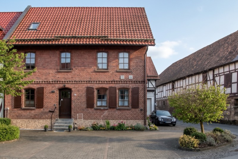 Backsteinhaus mit roten Fensterläden neben Fachwerkhäusern