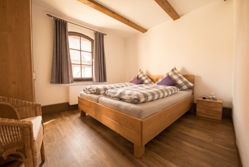 Schlafzimmer mit Holzdoppelbett, karierter Bettwäsche und Korbsessel