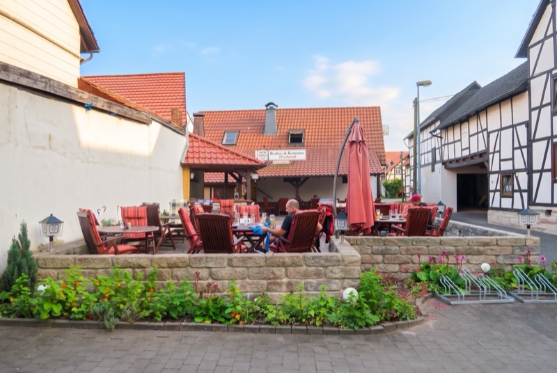 Sitzplätze mit Sonnenschirm vor dem Haus, eingefasst von Blumenbeeten